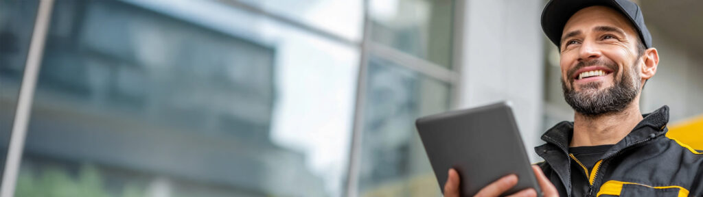 Smiling service professional using a tablet outside a modern building, representing organized job management and digital workflows.